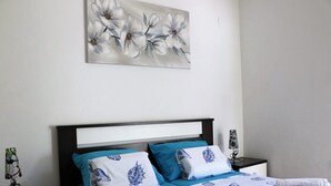 A neatly made bed with a floral wall art above, a nightstand with a lamp, and a blue and white patterned bedspread. - Apartment Marina (Punat)