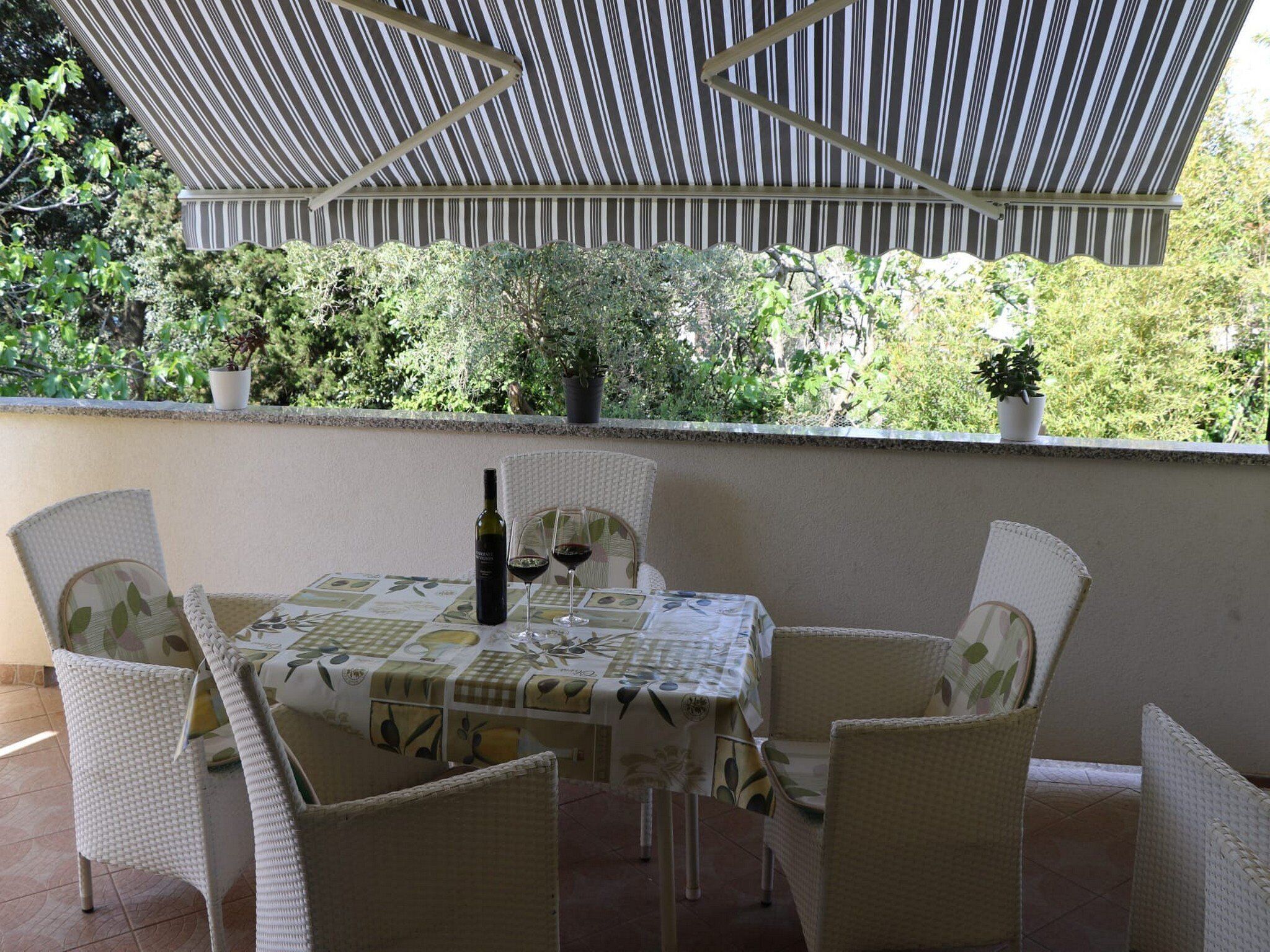 An outdoor patio with a table and chairs, a bottle of wine, and potted plants.