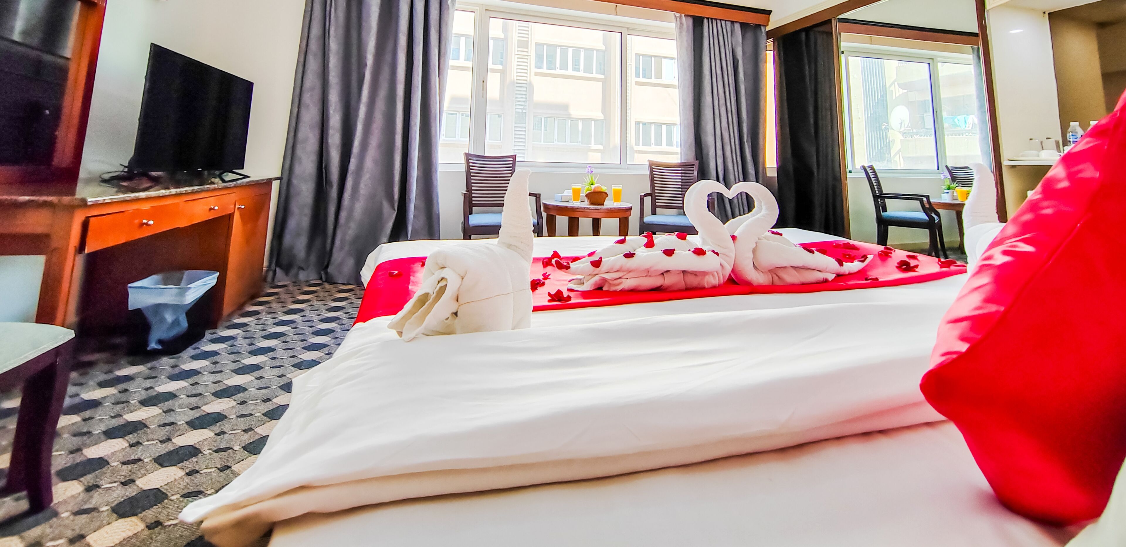 Una habitación de hotel con cama, televisión, escritorio y ventana con cortinas.