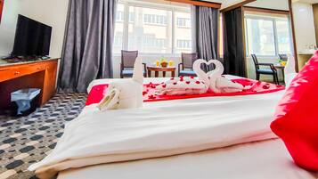 Una habitación de hotel con cama, televisión, escritorio y ventana con cortinas.