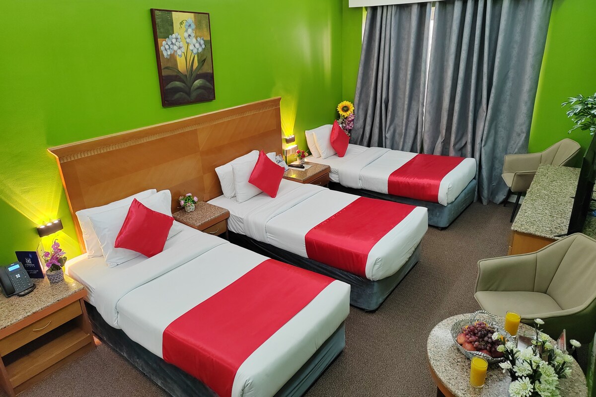 A hotel room with two beds, a nightstand, a chair, and a small table with fruit and drinks.