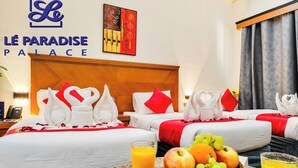 A hotel room with two beds, a headboard, a wall with the hotel name, a painting, and a fruit basket with a glass of orange juice. - Le Paradise Palace Hotel Deira Dubai Al Rigga (Dubai)