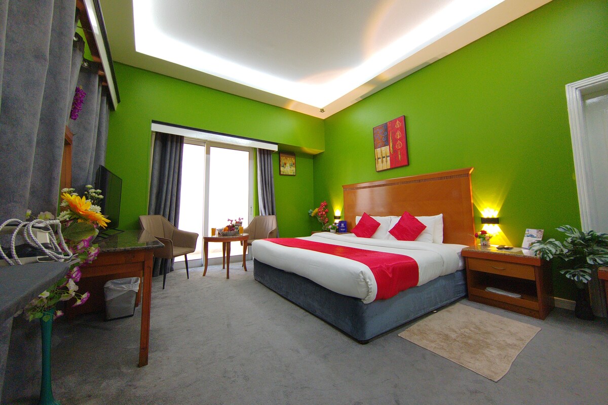 A hotel room with a bed, a desk, a chair, a TV, and a window with curtains.