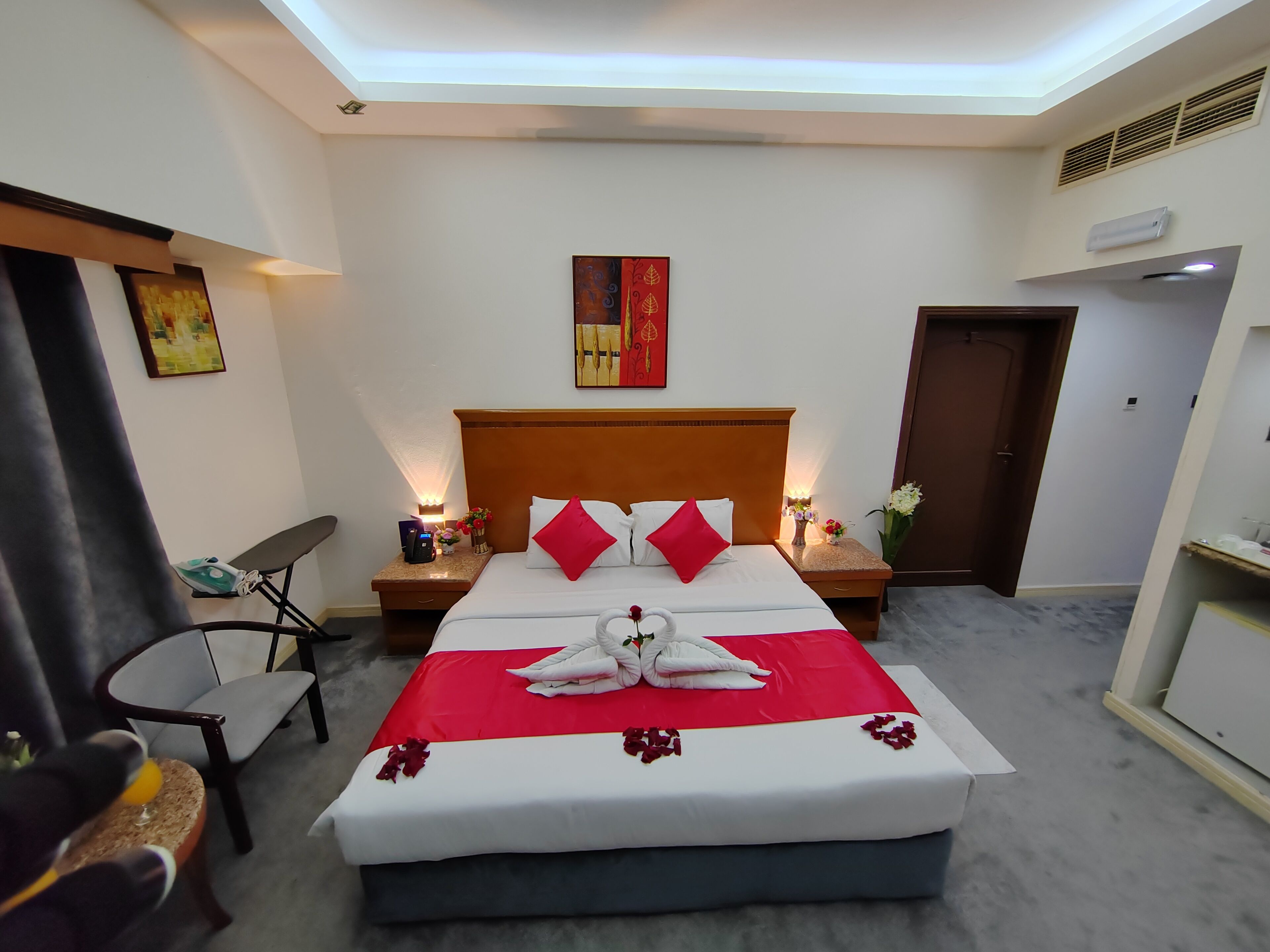 A hotel room with a neatly made bed, a nightstand with a lamp, a chair, and a door.