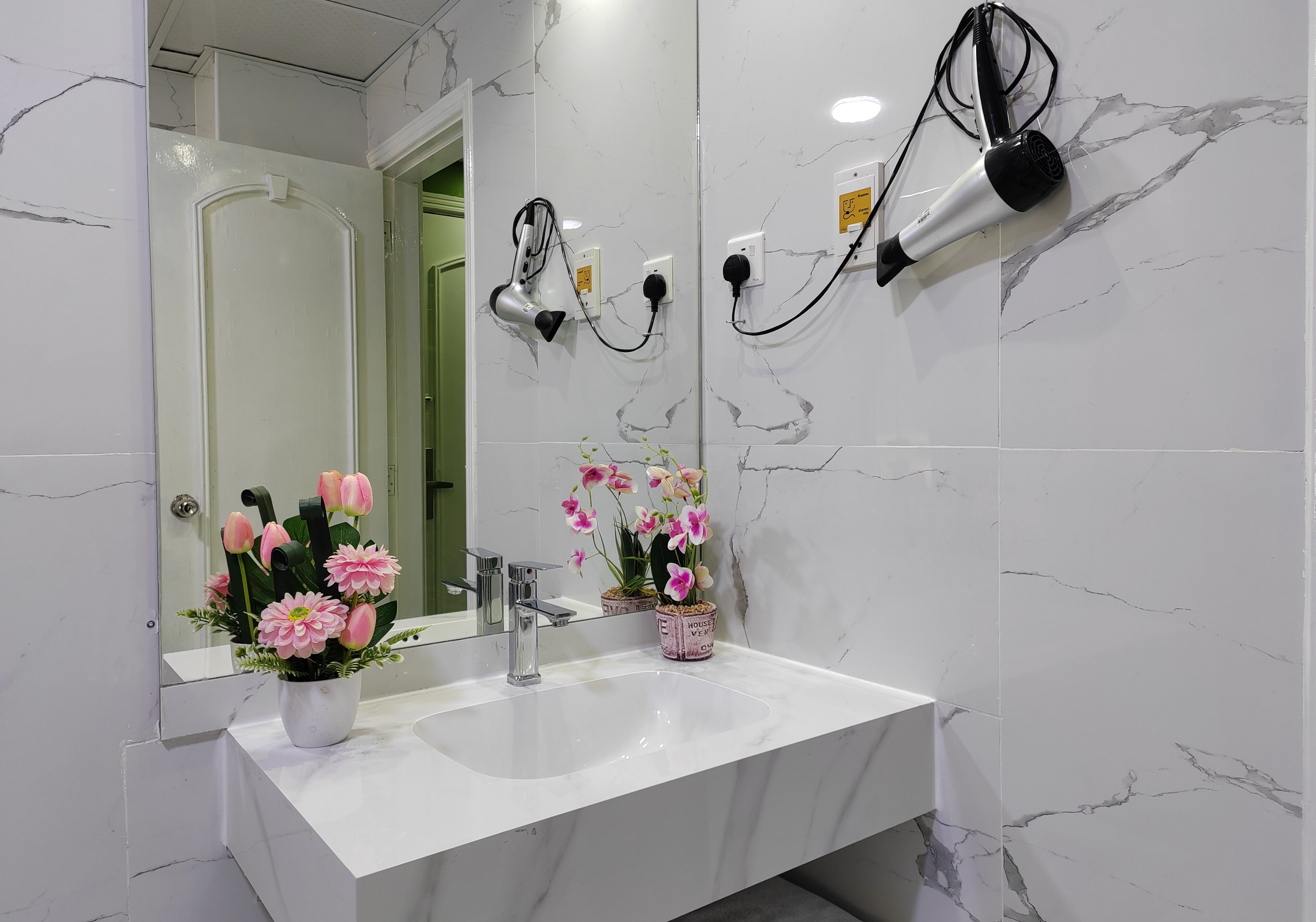 A bathroom with a white marble sink, a mirror, and two hair dryers mounted on the wall.