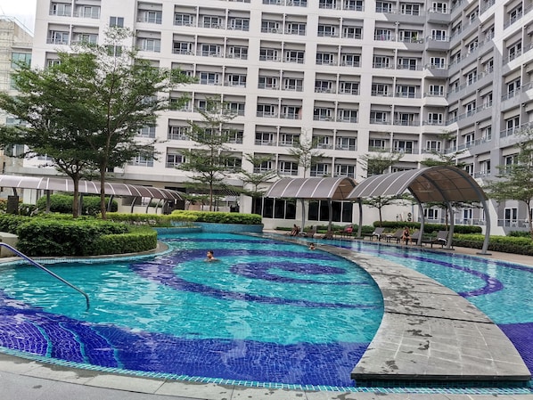 Enjoy a refreshing swim in the large circular pool surrounded by a beautifully maintained garden with hedges and trees.
