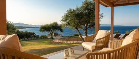 A covered outdoor seating area with wicker furniture and a view of the sea.