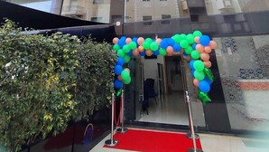 Een hotel ingang met een rode loper, een glazen gevel en een decoratieve boog van ballonnen.