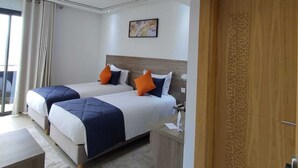 Een moderne hotelkamer met twee bedden, een houten deur met ingewikkelde decoraties, een groot raam met gordijnen en een schilderij aan de muur.