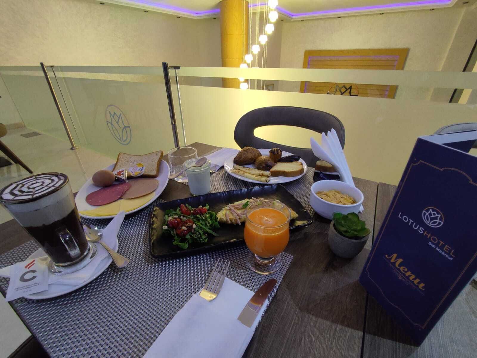 Un desayuno con diversos alimentos, un menú y un vaso de zumo de naranja sobre una mesa.