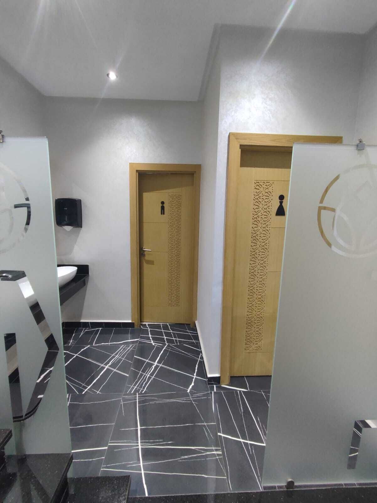 A restroom with a black and white marble floor, a wooden door with a decorative panel, and a white sink.