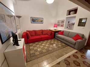 A living room with a red sofa, a grey sofa, a patterned rug, and a television. - Entire apartment fully equipped. Ideal for families or for work. (Palermo)