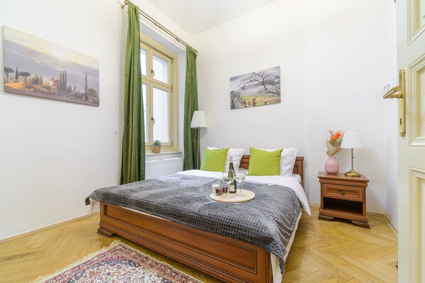 A bedroom with a wooden bed, green curtains, a nightstand with a lamp, and two wall-mounted paintings. - 3-bedrooms apartment in center of Prague (Prague)