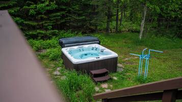 A hot tub in a forested area with a wooden deck in the foreground.