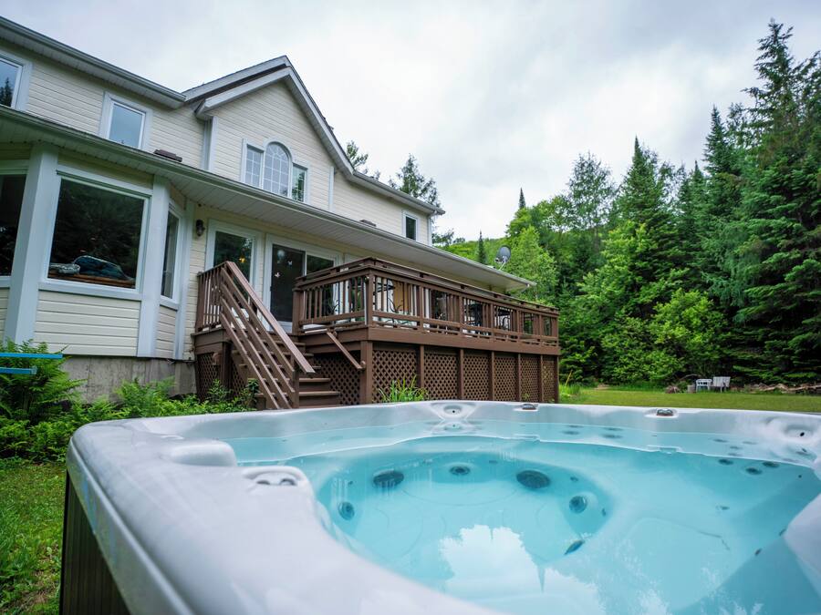 Een hottub in een achtertuin met een houten terras en een huis op de achtergrond.