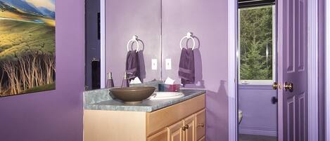 A bathroom with a large mirror, a sink, and a window.