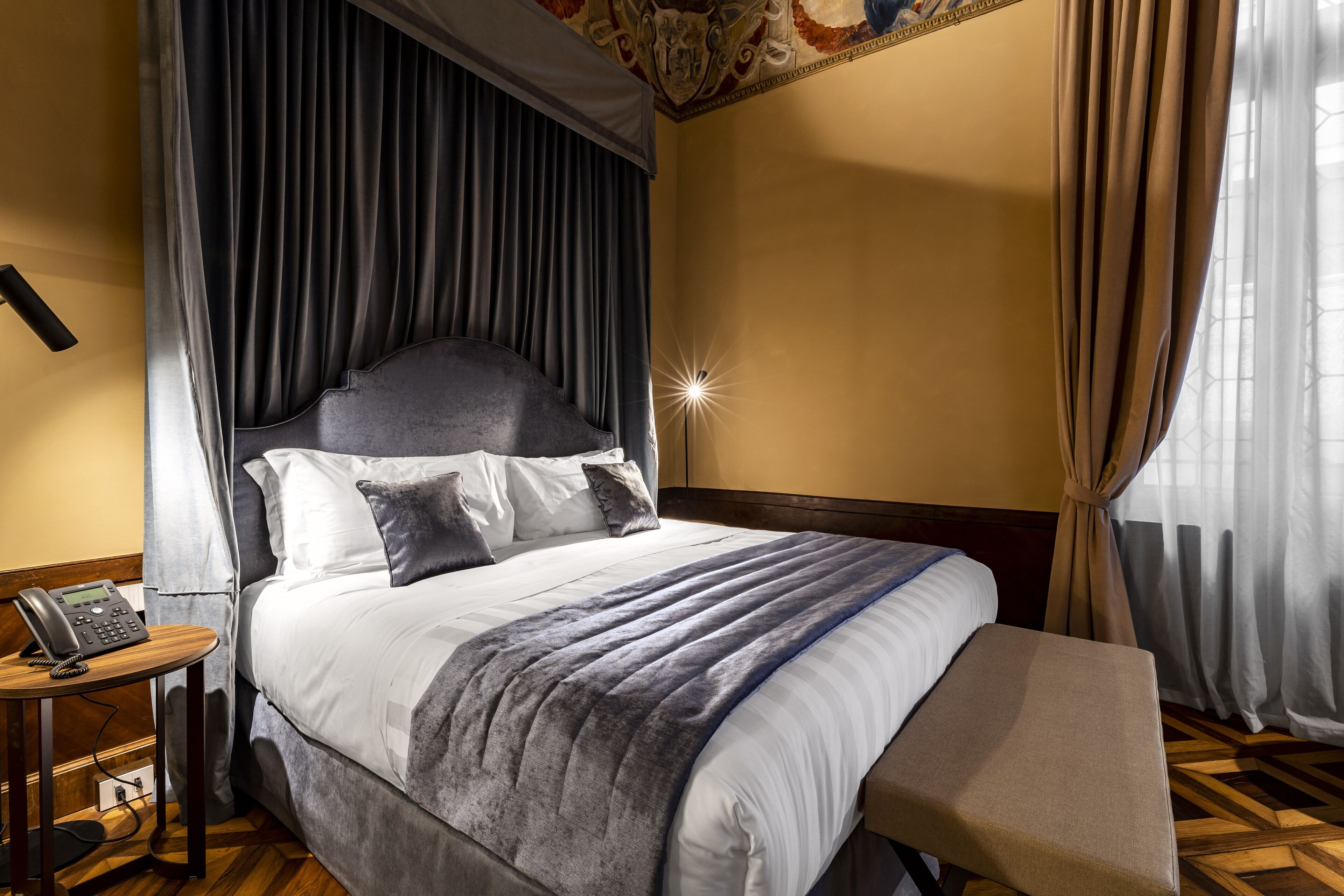 A neatly made bed with a headboard, a bedside table with a phone, and a bench at the foot of the bed.