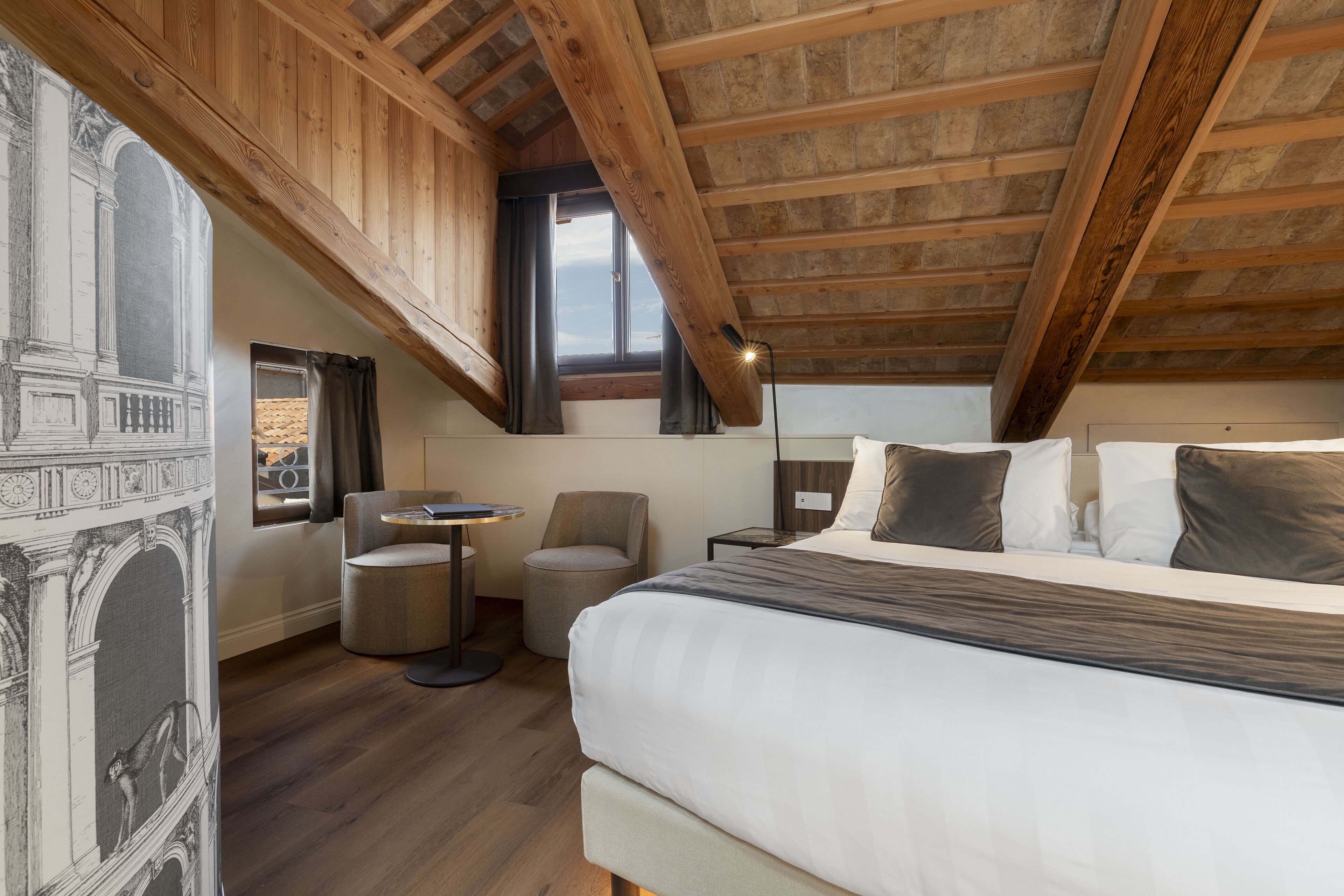 Un dormitorio con una cama grande, una mesita redonda pequeña, una silla y una ventana con cortinas.