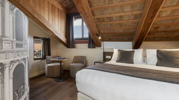 Un dormitorio con una cama grande, una mesita redonda pequeña, una silla y una ventana con cortinas.