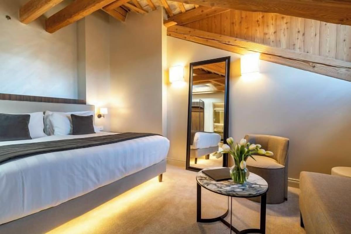 A bedroom with a bed, bedside table, chair, and a mirror.