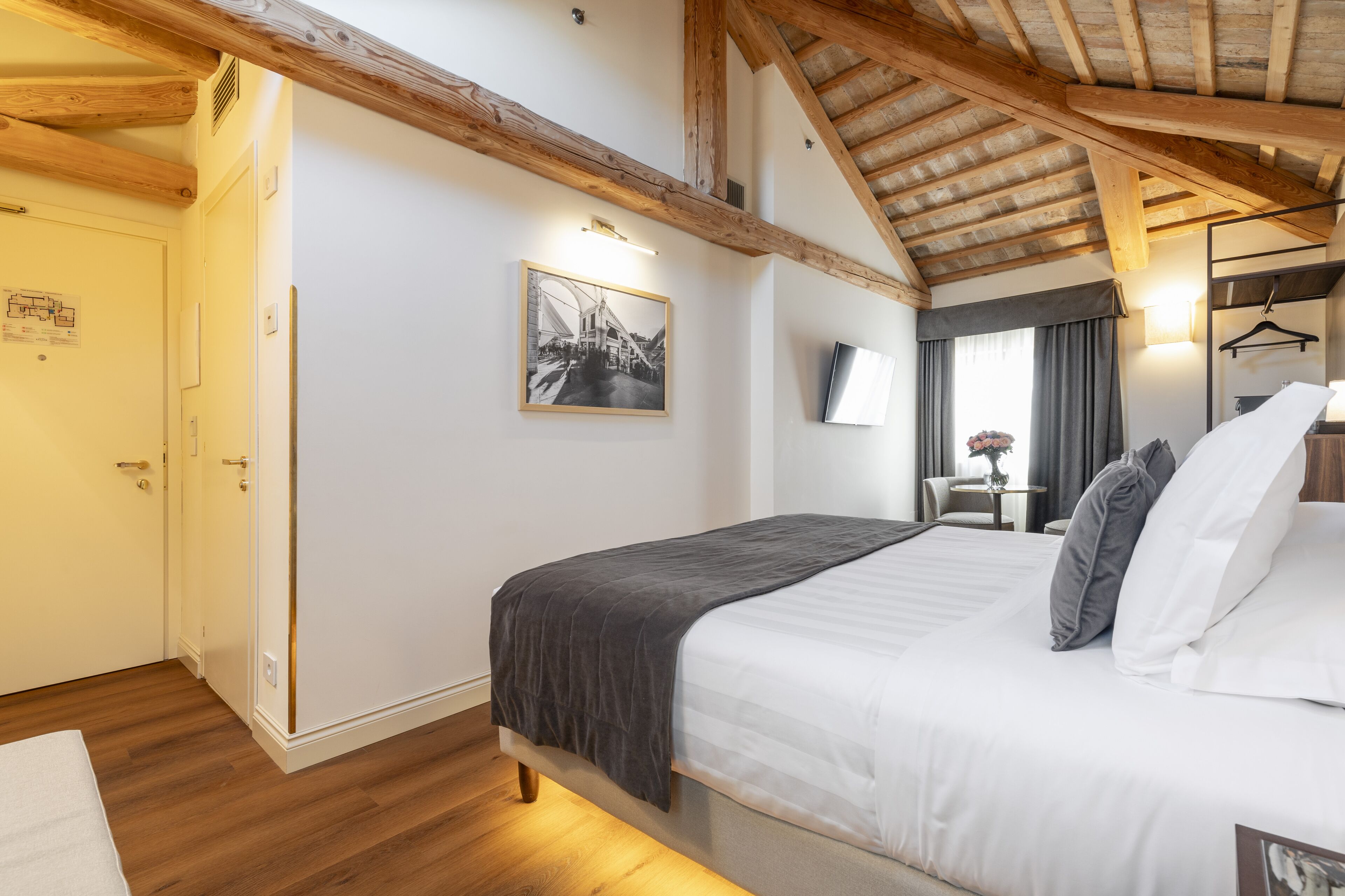 A bedroom with a bed, wooden beams, a framed picture, a TV, and a desk with a chair.