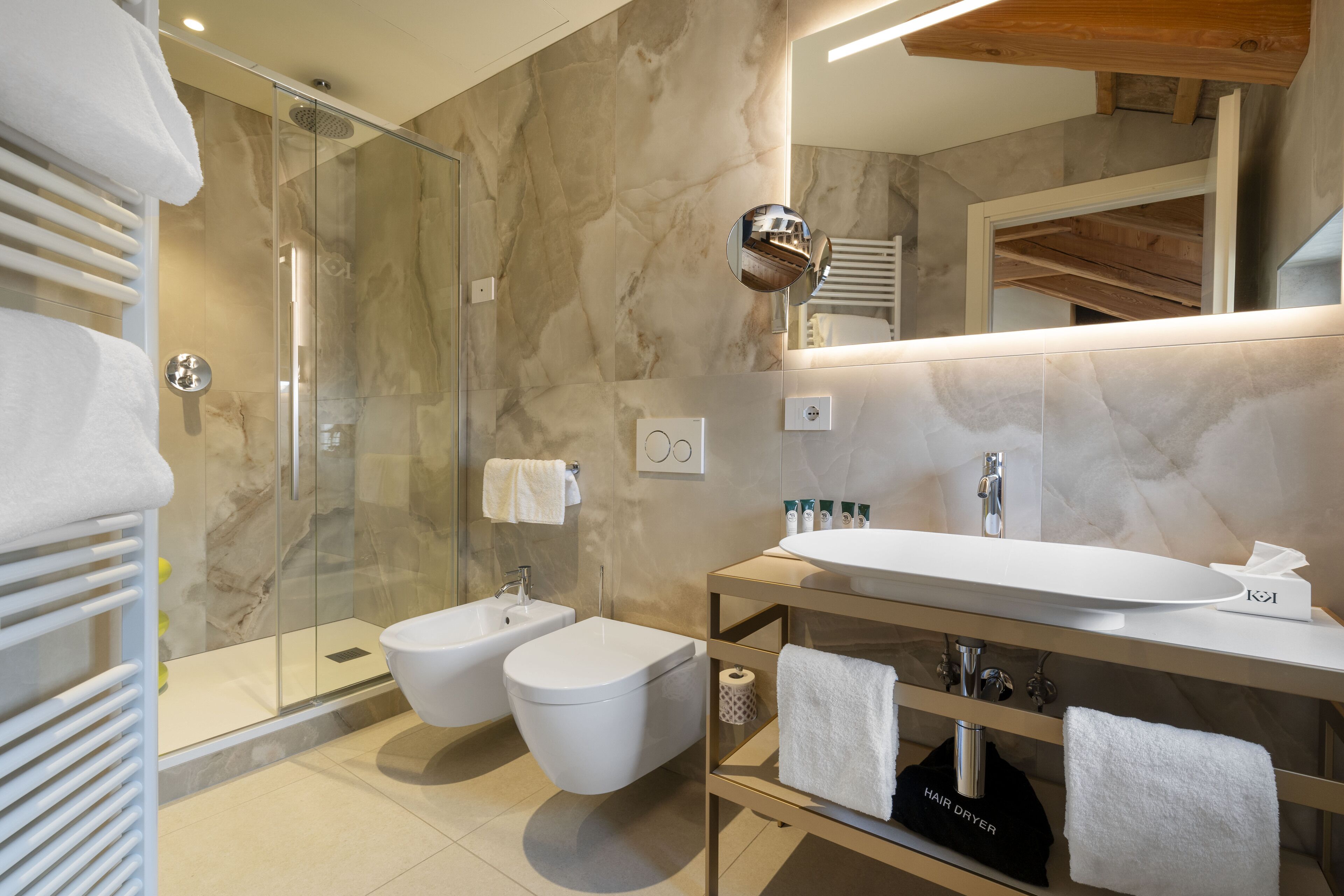 Ein modernes Badezimmer mit Duschkabine aus Glas, einem Bidet, einem Waschbecken mit Spiegel und einem Handtuchhalter.