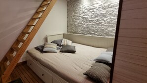 Un dormitorio con techo inclinado, una escalera de madera, cama con almohadas, un radiador y pared texturizada.
