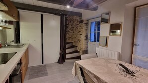 Cocina compacta con un lavamanos, una mesa de comedor con mantel de encaje, y una escalera que lleva a otra habitación.