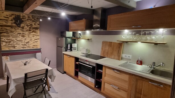 Una cocina compacta con pared de piedra, armarios de madera, horno empotrado y comedor con mesa y sillas.
