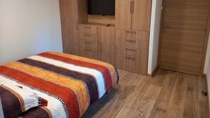 A bedroom with a bed, a wooden wardrobe with a TV shelf, and a door. - VILLA LA TREILLE (Saint-Maximin-la-Sainte-Baume)