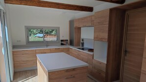 A modern kitchen with wooden cabinets, a white countertop, and a window providing natural light. - VILLA LA TREILLE (Saint-Maximin-la-Sainte-Baume)