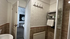 A bathroom with a shower, a sink, and a mirror. There is a towel rack on the wall and a toilet visible in the background.