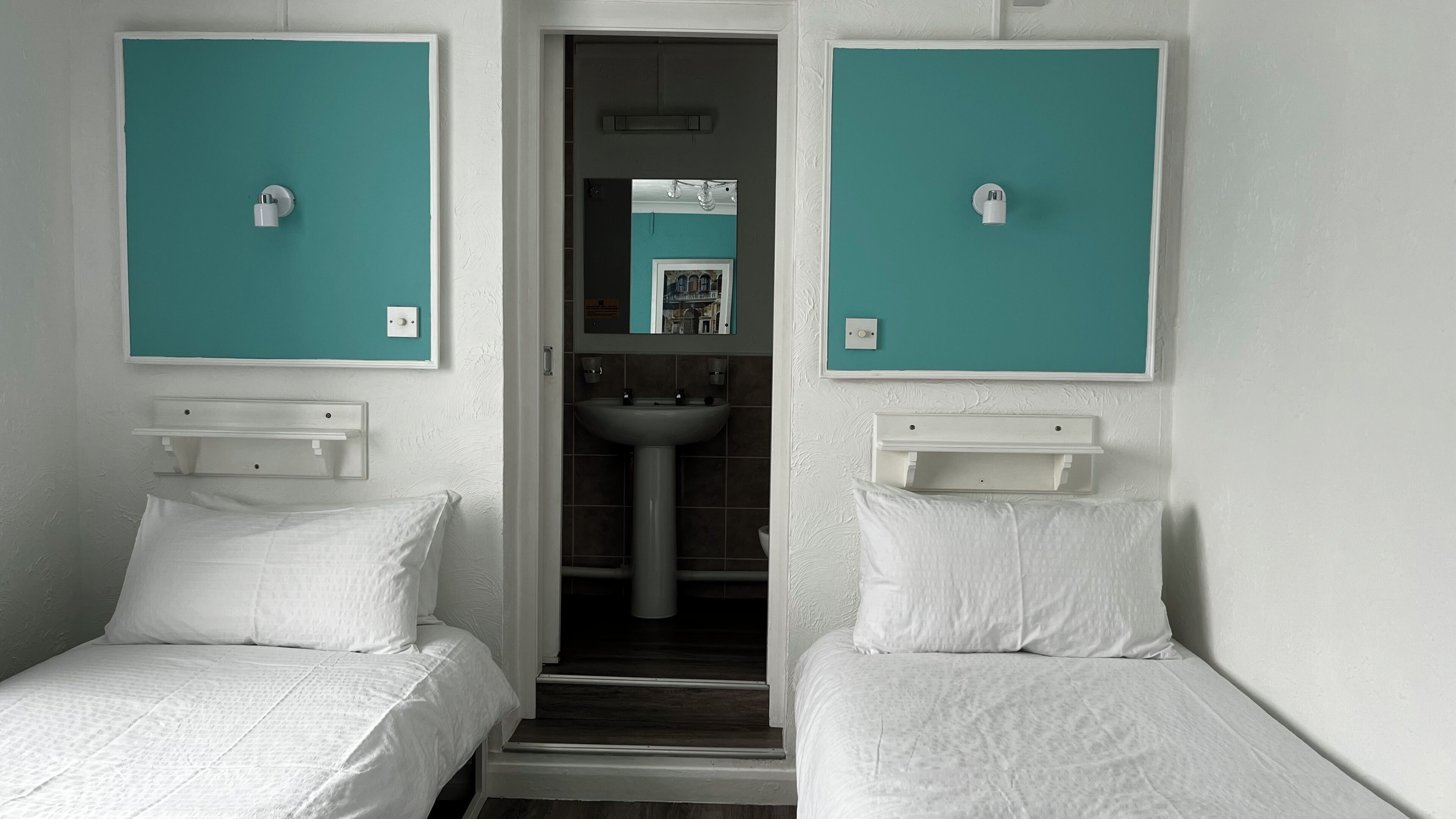 A room with two single beds, a small bathroom with a sink, and a mirror.