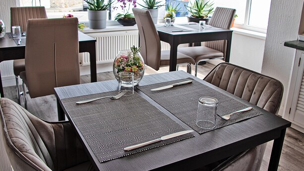 A dining area with a table set for four, including a vase with flowers, a glass of water, and cutlery.