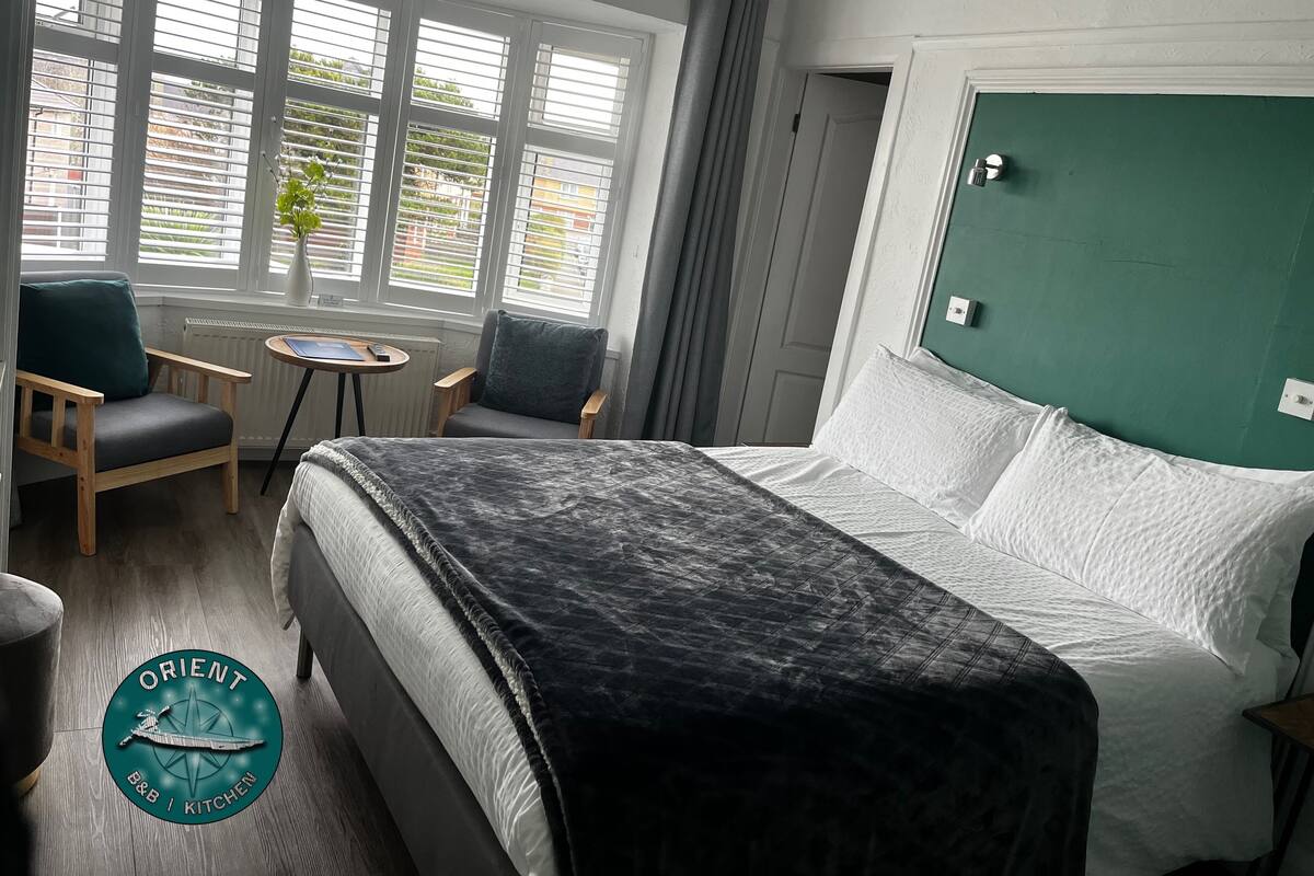 A hotel room with a bed, two armchairs, a small table, and a window with blinds.