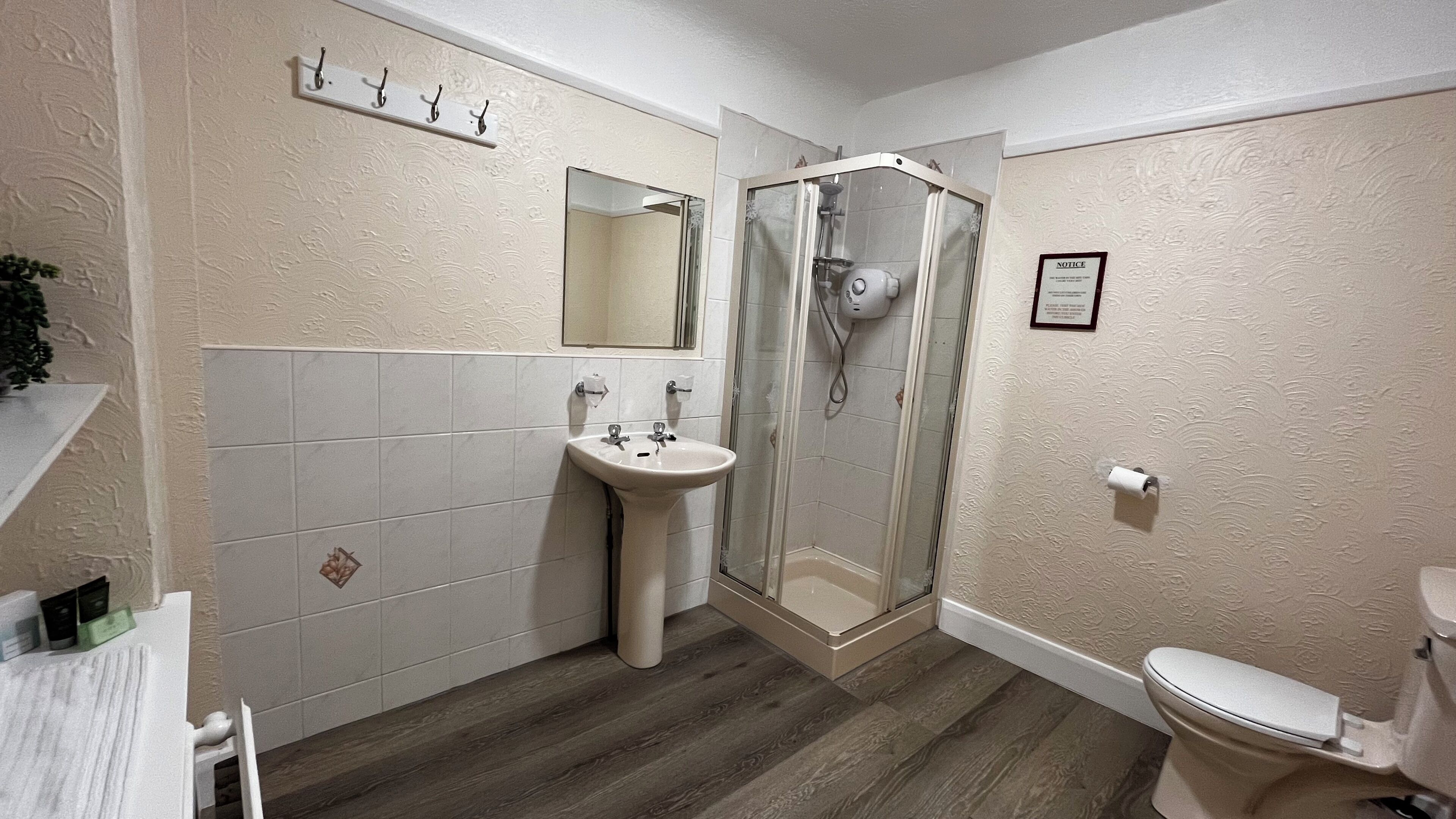 A bathroom with a shower, sink, toilet, and a notice on the wall.
