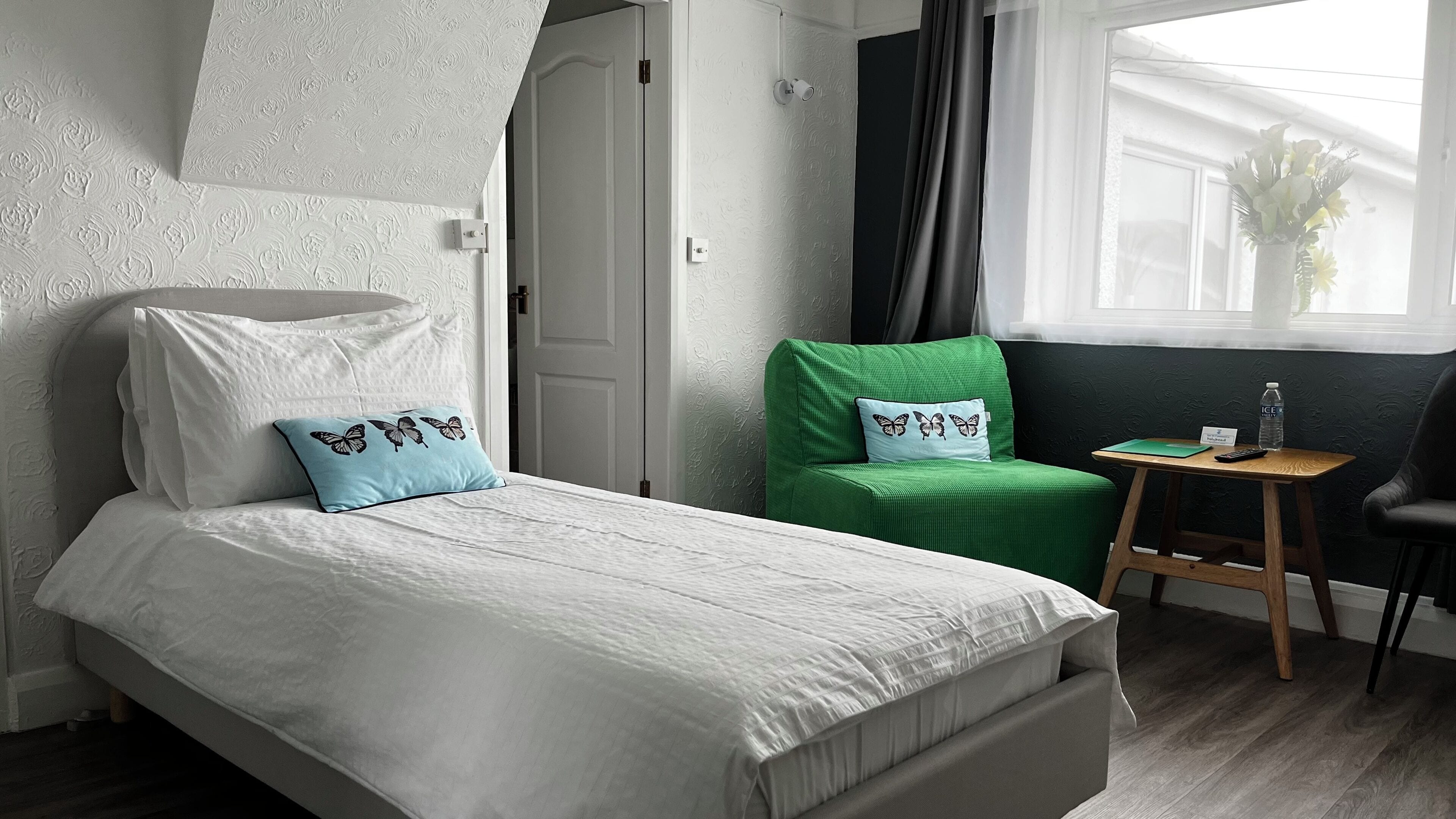 A neatly arranged hotel room with a bed, a green chair, a small table, and a window with a view.