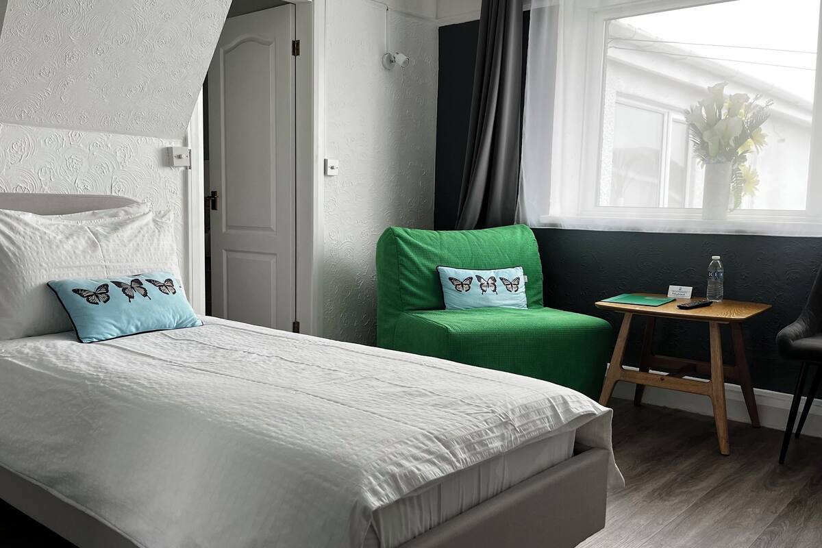 A neatly arranged hotel room with a bed, a green chair, a small table, and a window with a view.