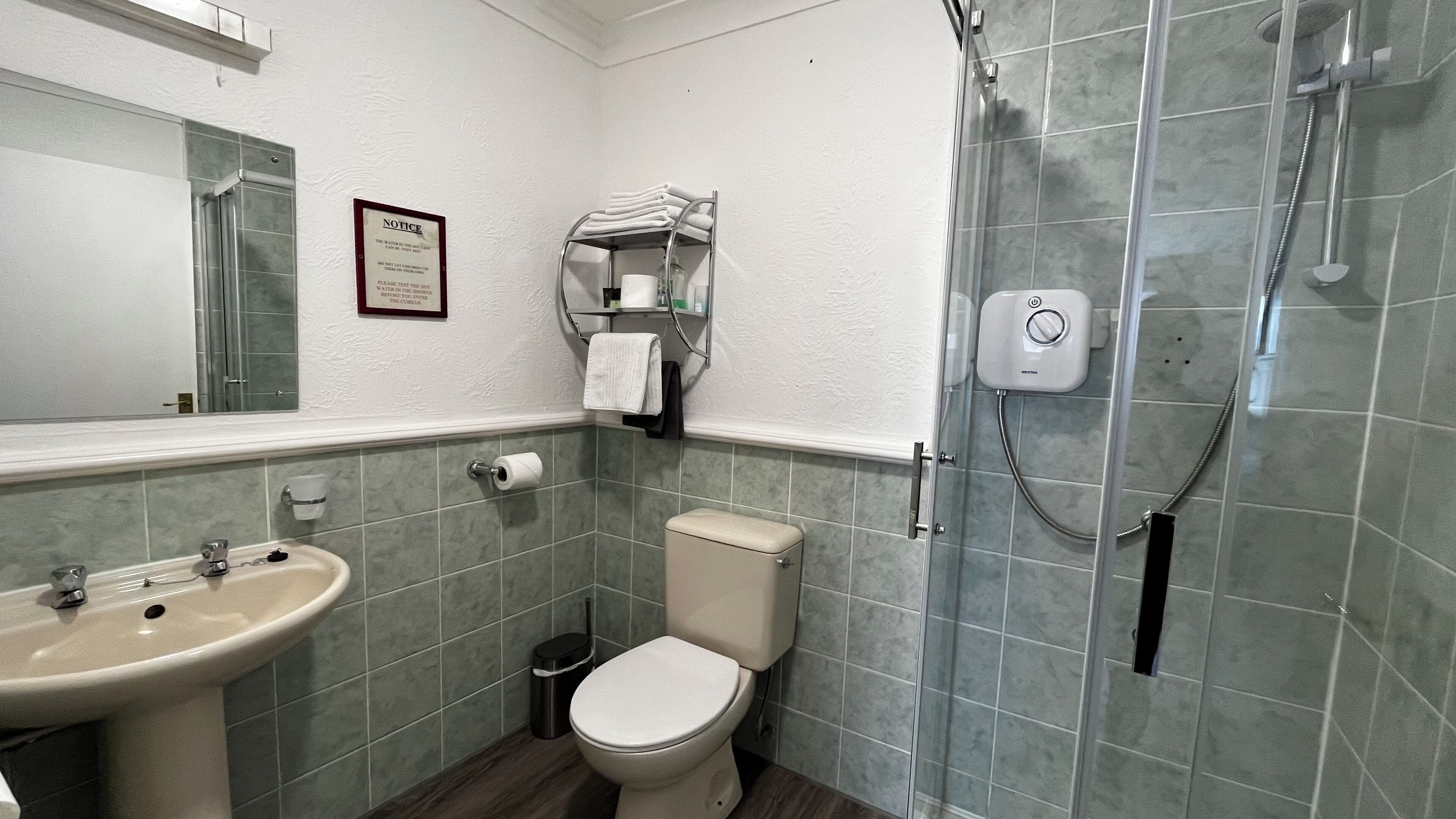 Un baño con lavamanos, inodoro, ducha y un aviso en la pared.