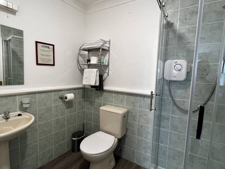 Un baño con lavamanos, inodoro, ducha y un aviso en la pared.