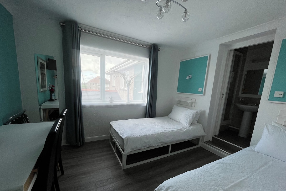 A small, clean room with two single beds, a desk, and a window with curtains.