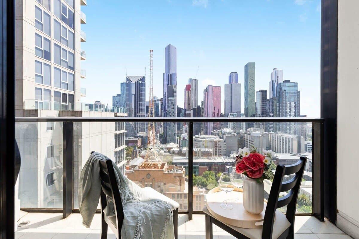 A balcony with a city view, a chair, a table with a vase of flowers, and a jacket hanging on the railing.