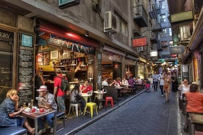 Una calle estrecha con mesas y sillas en terrazas de varios cafés y restaurantes.