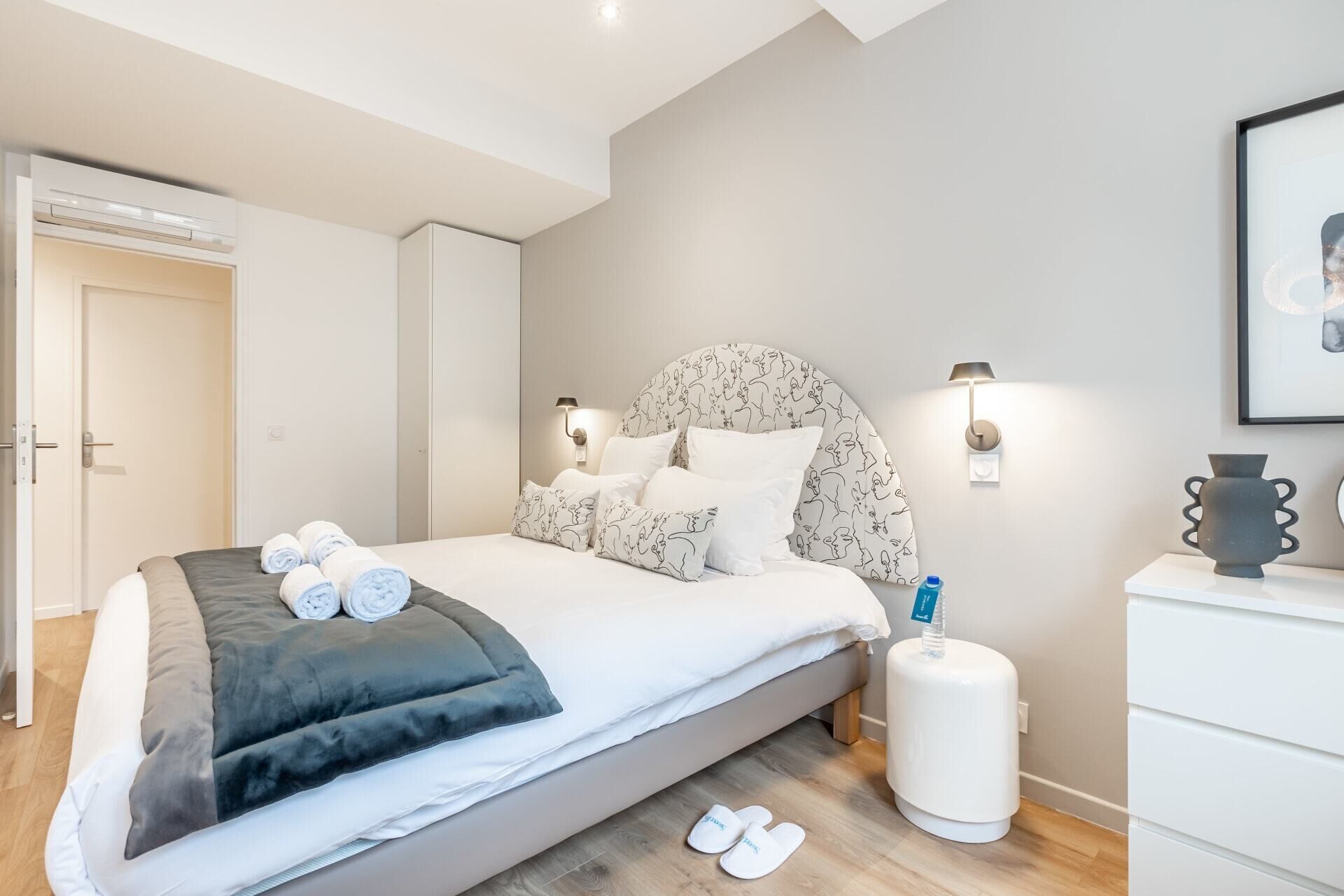 Une chambre à coucher moderne avec un lit, des tables de chevet, une commode et une lampe fixée au mur.