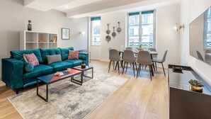 A modern living room with a teal sofa, a coffee table, and a dining area with checkered chairs.