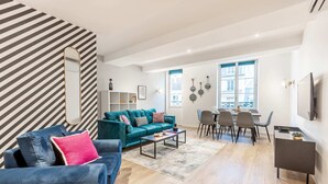 A modern living room with a teal sofa, a blue armchair, and a dining area with a table and chairs.