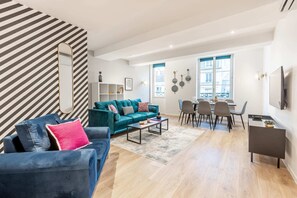 Uma sala de estar moderna com um sofá verde-água, uma poltrona azul e um espaço de jantar com mesa e cadeiras.