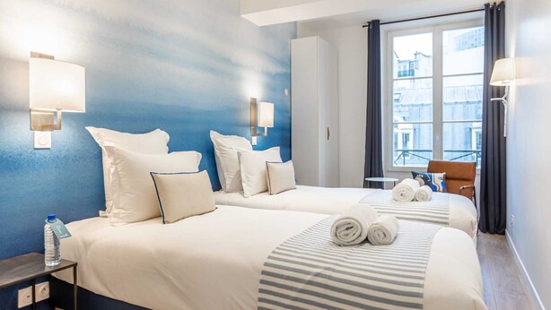 A hotel room with two beds, a small table, and a chair.