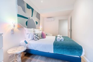 Quarto moderno com cama, almofadas, mesa de cabeceira e luminária fixada na parede.