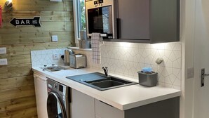 A compact kitchen with a washing machine, a sink, a microwave, and a bar sign. - Royal Snug & WEE Snug (Aboyne)